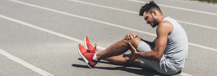 A man holding his knee in pain. He is sitting on a track.