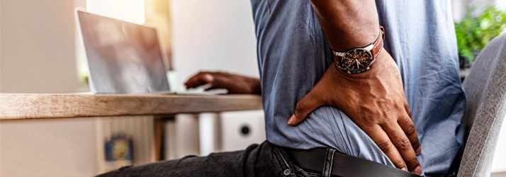 A man holding his lower back while sitting in a computer chair.